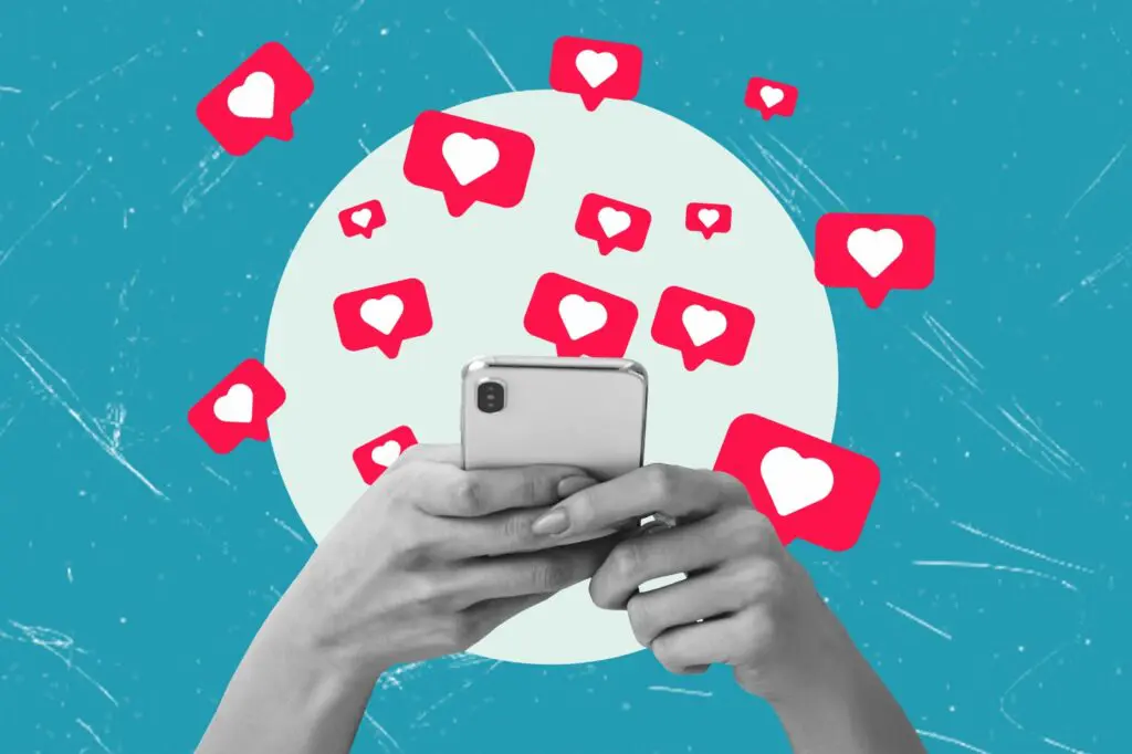 Hands holding a mobile phone with social media heart react badges flying out of it.