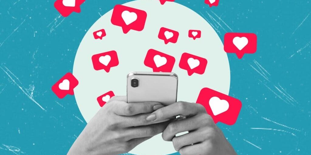 Hands holding a mobile phone with social media heart react badges flying out of it.